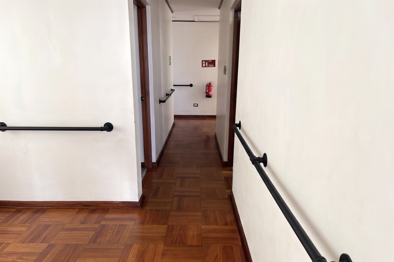 Pasillo de la residencia con pasamanos a ambos lados y piso de parqué